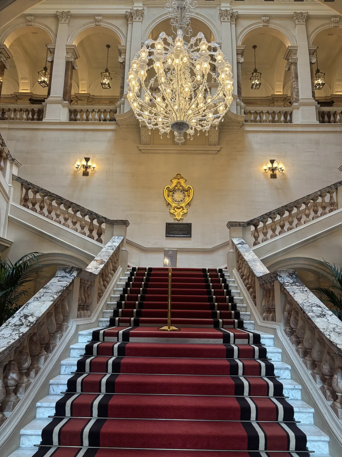 The grand marble staircase at Raffles London at The OWO with red carpet and Murano chandelier